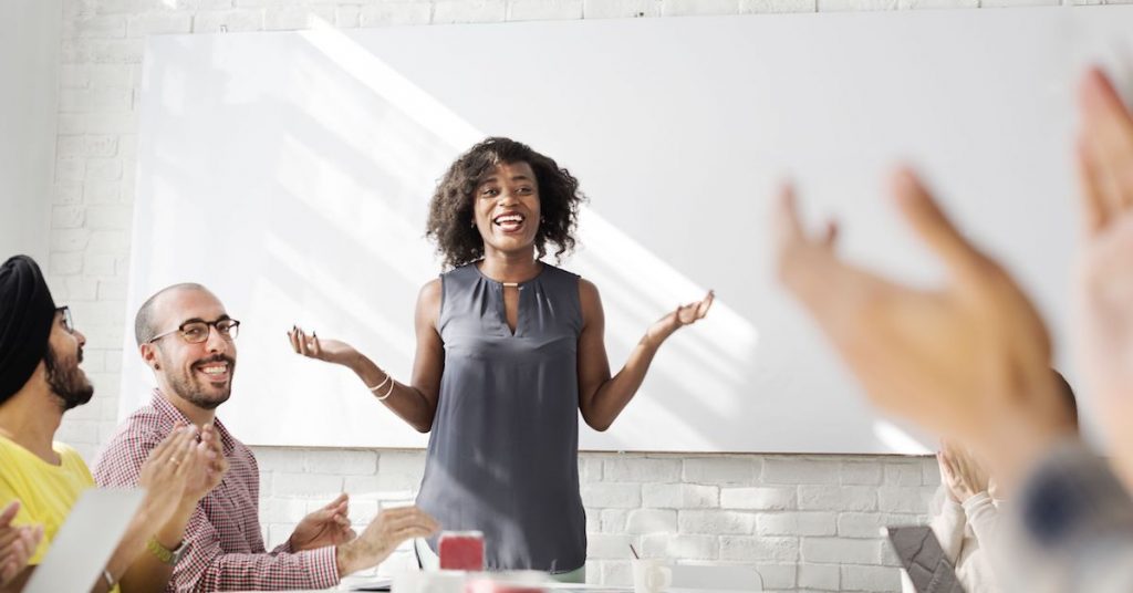 A group of diverse co-workers celebrating a presenter at a board meeting.